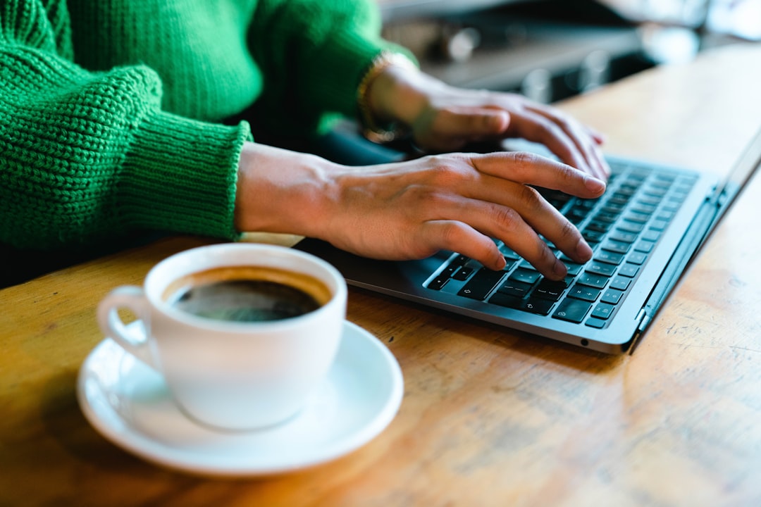 A person typing on a laptop with a cup of coffee